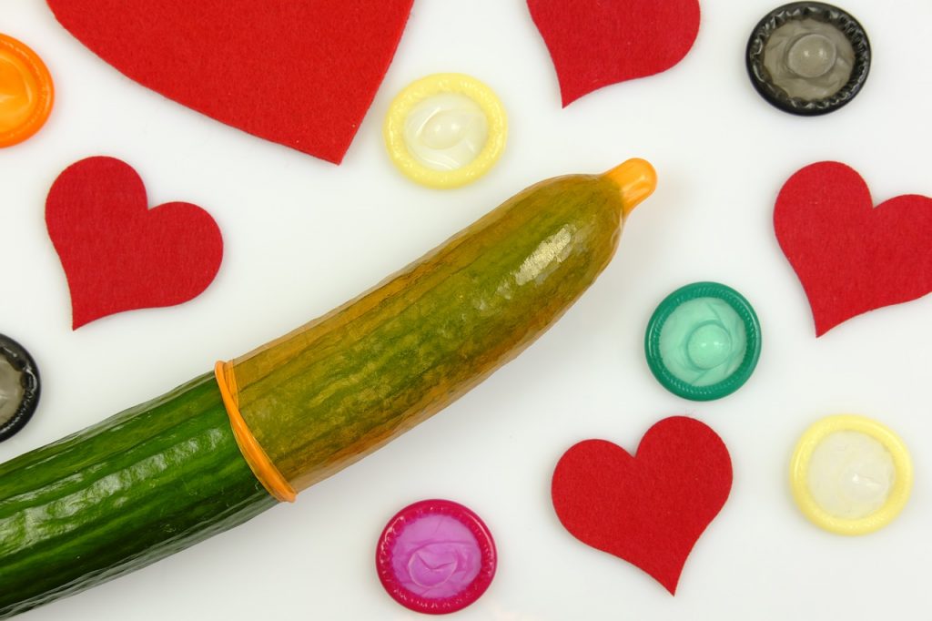 Cucumber wrapped in orange condom covered by felt hearts and condoms.