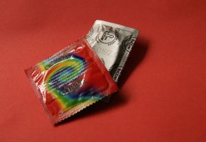 Two colorfully wrapped latex condoms against a red background