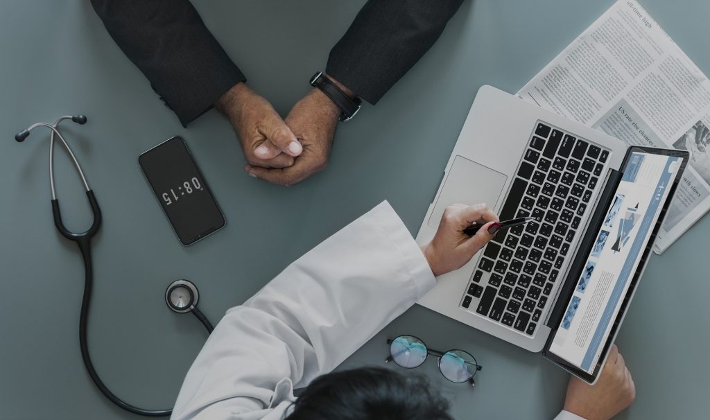 Amedical doctor points to a laptop screen to explain chlamydia testing to a patient