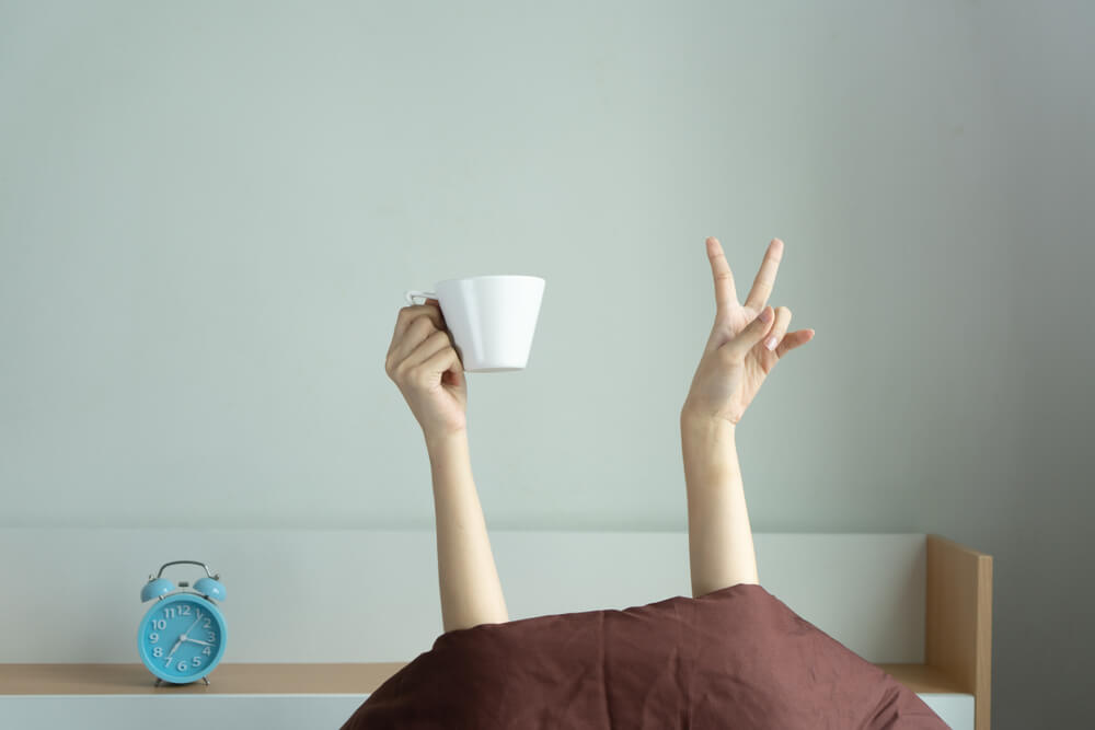 Woman showing funny v sign holding blue tea cup relaxing in bed room, Young woman with two hands drinking coffee in blue cup after awaking. consent is like tea analogy concept.